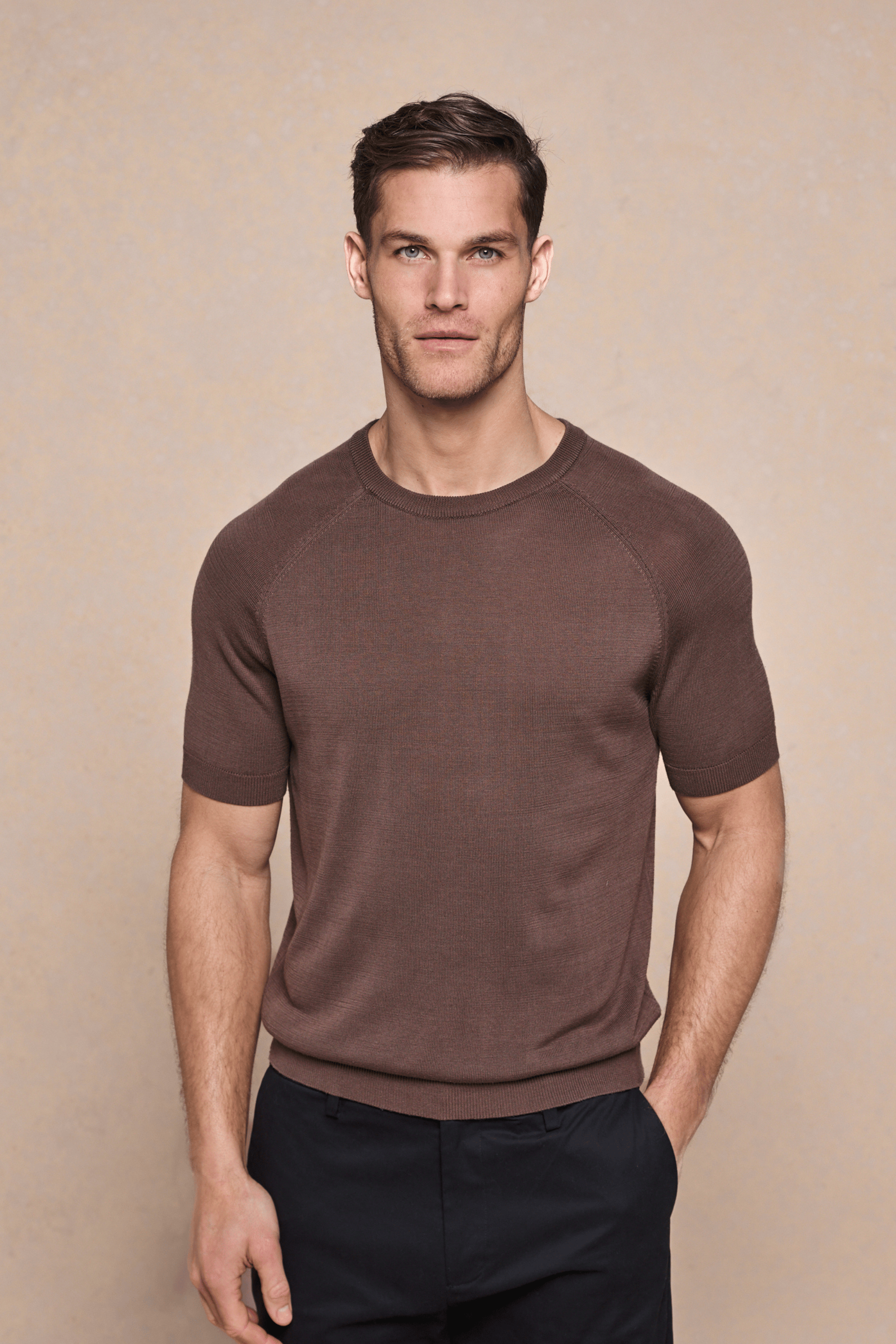 Man wearing a brown Riera Knit Crew Neck T-Shirt with ribbed details and black trousers.