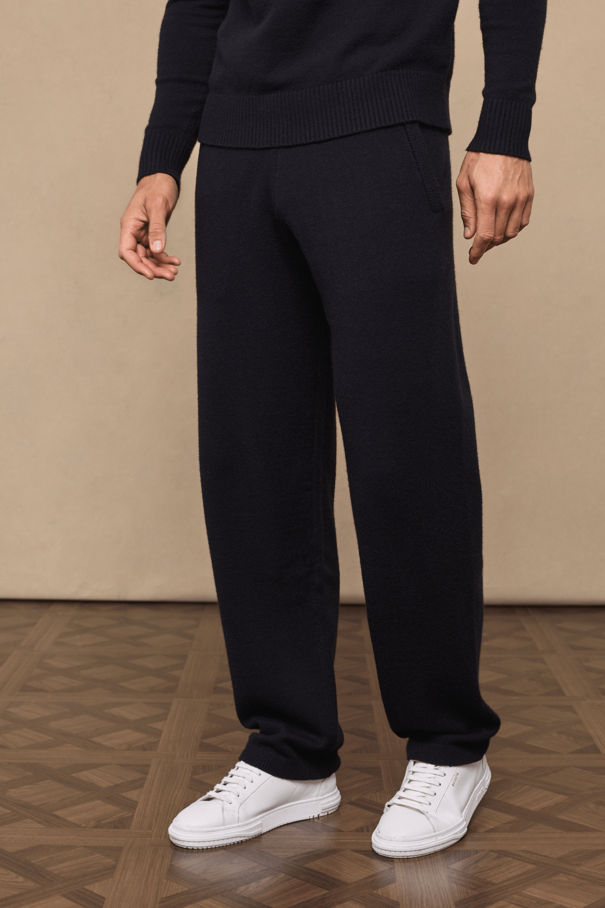 Man wearing black Rowan Knitted Trousers with side pockets and a matching sweater, paired with white sneakers.
