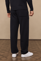Rear view of a person wearing black Rowan knitted trousers with a back pocket and adjustable drawcords.