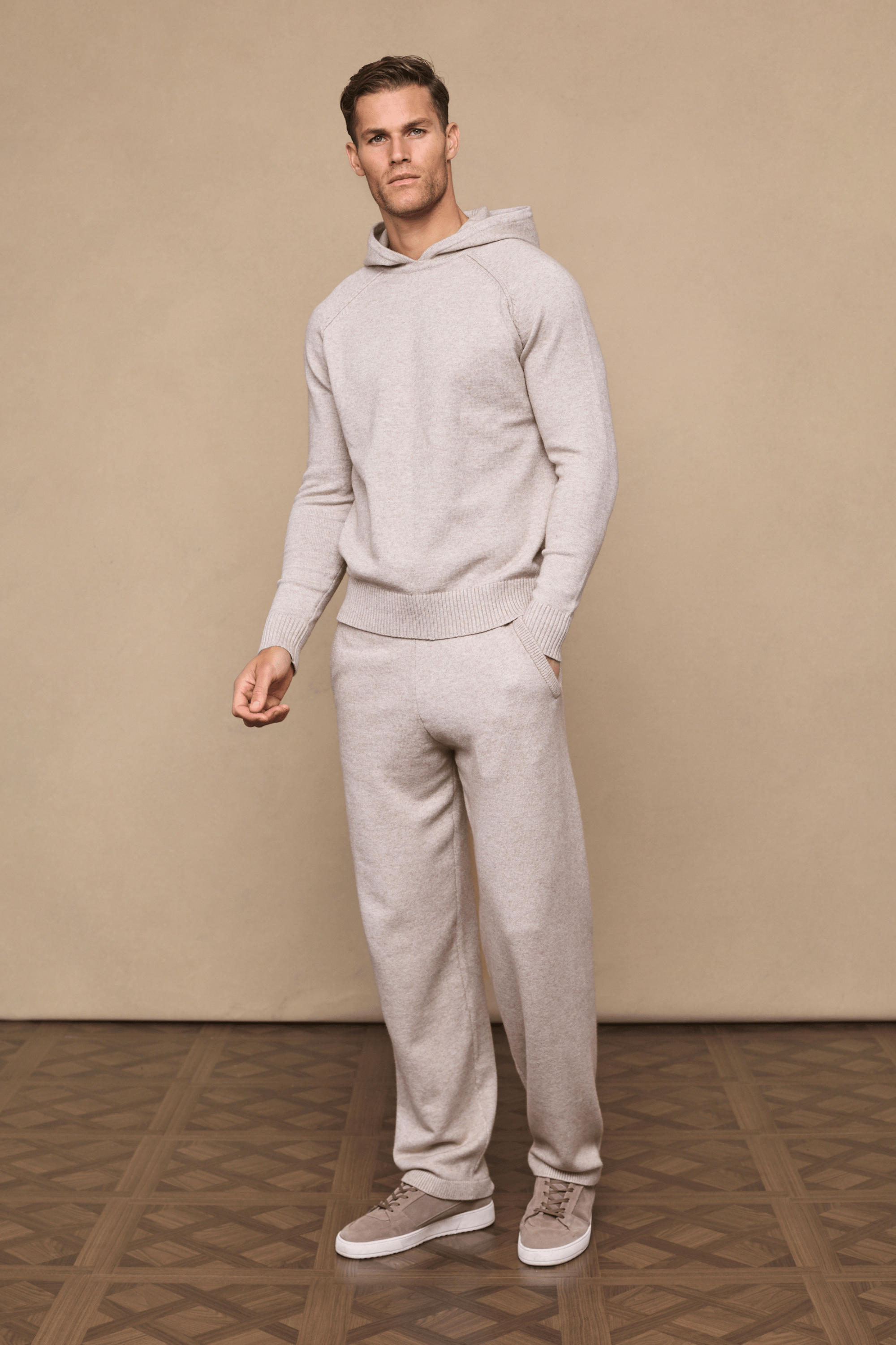 Man wearing a full Rowan Knitted Trouser and Hoodie set in oatmeal, with side pockets and drawcords.