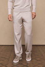 Man wearing oatmeal knitted trousers and matching sweater, with side pockets and drawcords, paired with beige sneakers.