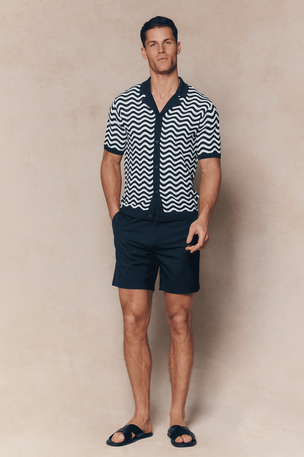 Man in Serenita Ecru/Navy knitted shirt with wavy pattern, open collar, and navy shorts.