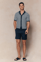 Man in Serenita Ecru/Navy knitted shirt with wavy pattern, open collar, and navy shorts.