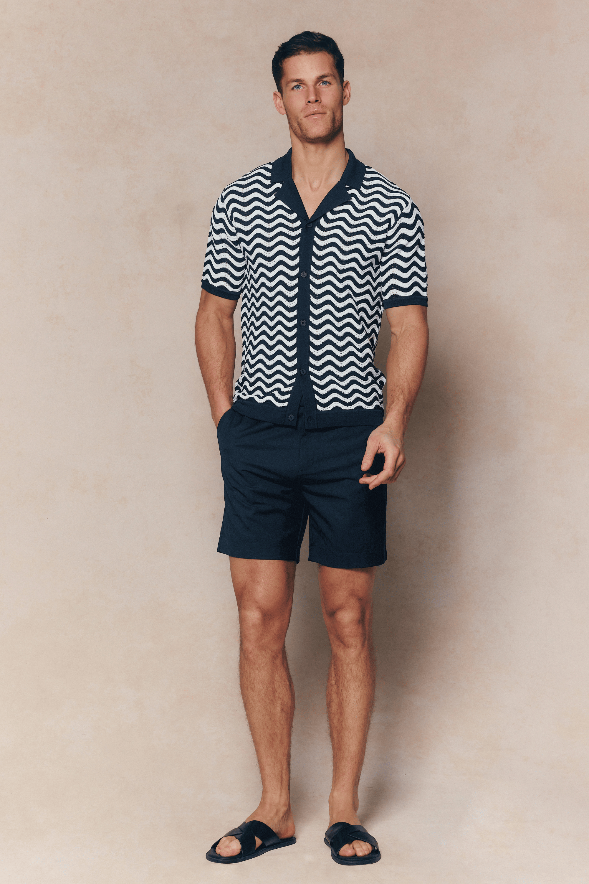 Man in Serenita Ecru/Navy knitted shirt with wavy pattern, open collar, and navy shorts.