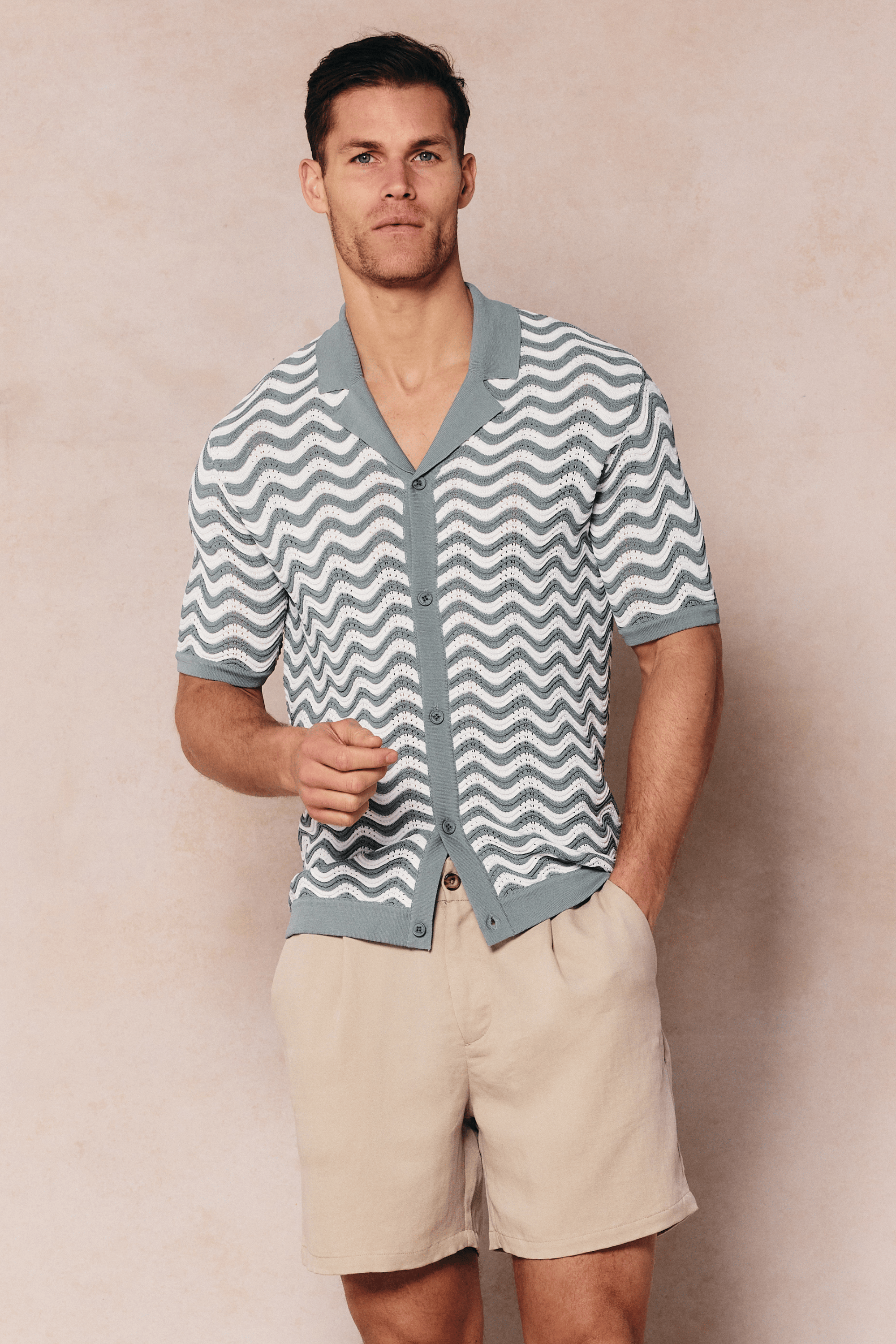 Man wearing a sage/white Serenita knitted shirt with a wave pattern, open collar, and button-through front.