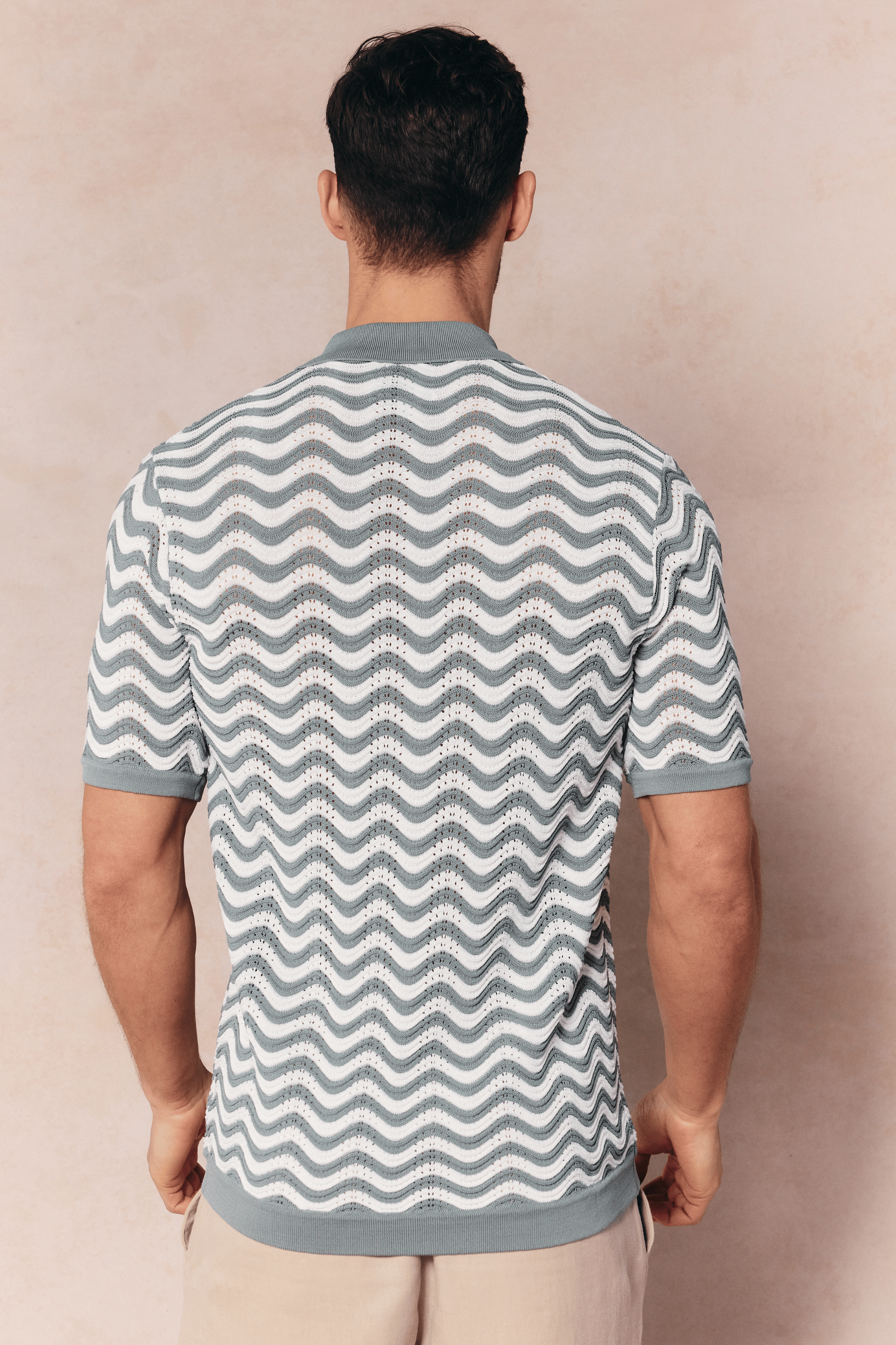 Man from behind wearing a Serenita knitted shirt in sage/white with a wave pattern and short sleeves.