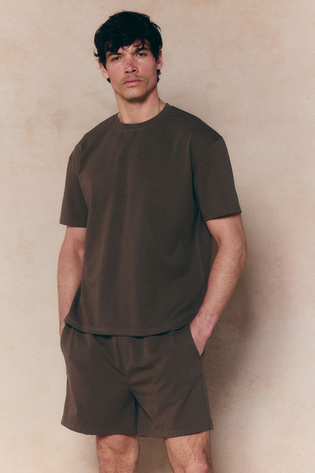 Man wearing dark brown Tomas elasticated waist shorts and matching t-shirt, relaxed fit, crinkled texture.