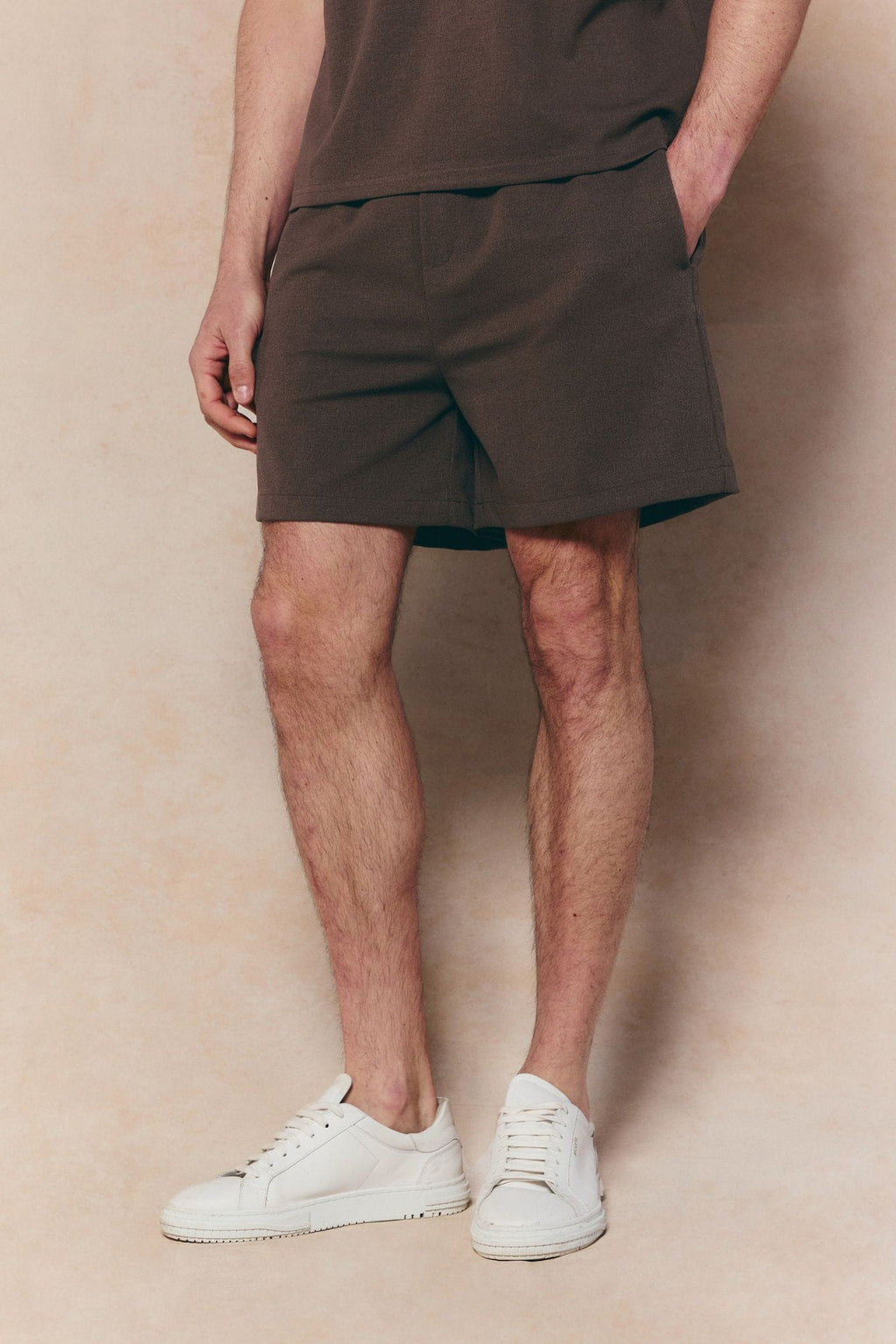 Man wearing dark brown Tomas elasticated waist shorts with a subtle crinkled texture, paired with white sneakers.