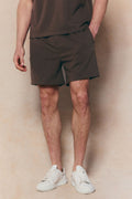 Dark brown Tomas elasticated waist shorts with crinkled texture, worn by a person in white sneakers.