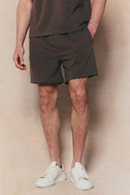 Dark brown Tomas elasticated waist shorts with crinkled texture, worn by a person in white sneakers.