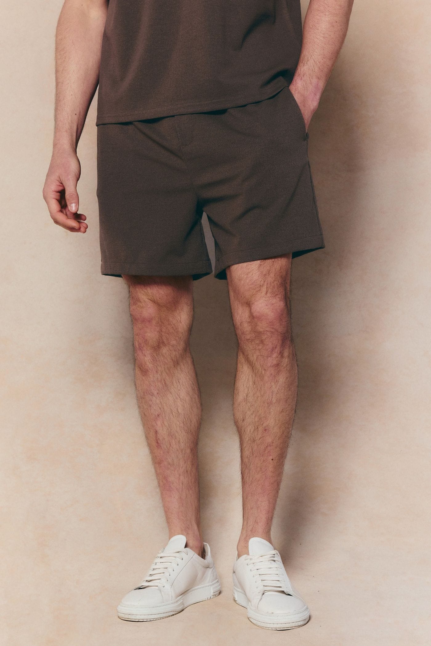 Dark brown Tomas elasticated waist shorts with crinkled texture, worn by a person in white sneakers.