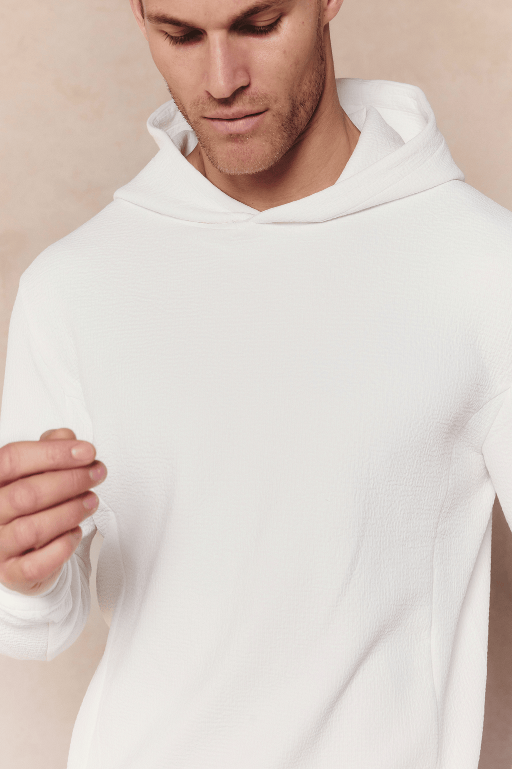 Man wearing an ivory Zarco Crinkled Jersey Hoodie with a textured fabric and hood.