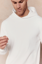 Man wearing an ivory Zarco Crinkled Jersey Hoodie with a textured fabric and hood.