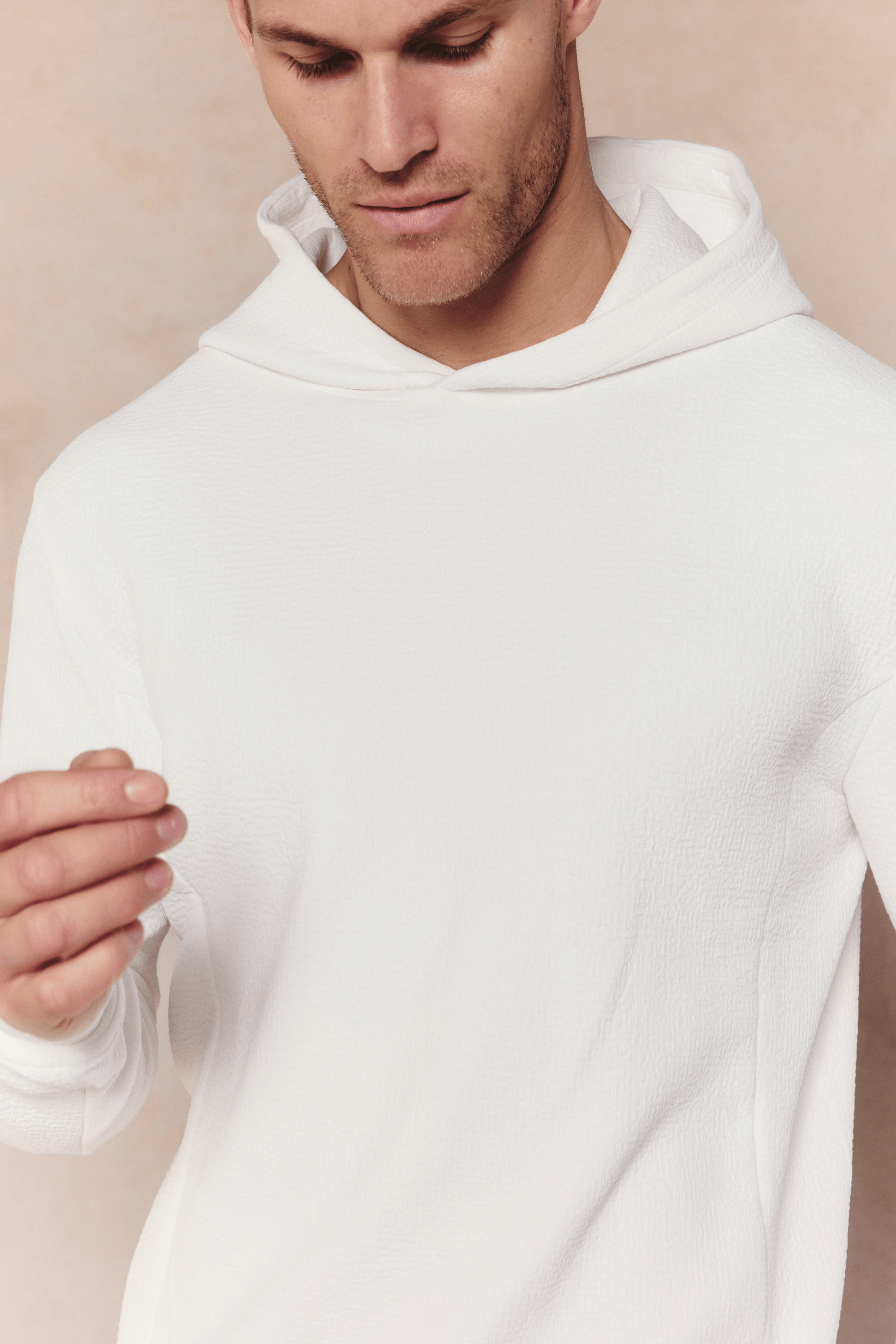 Man wearing an ivory Zarco Crinkled Jersey Hoodie with a textured fabric and hood.