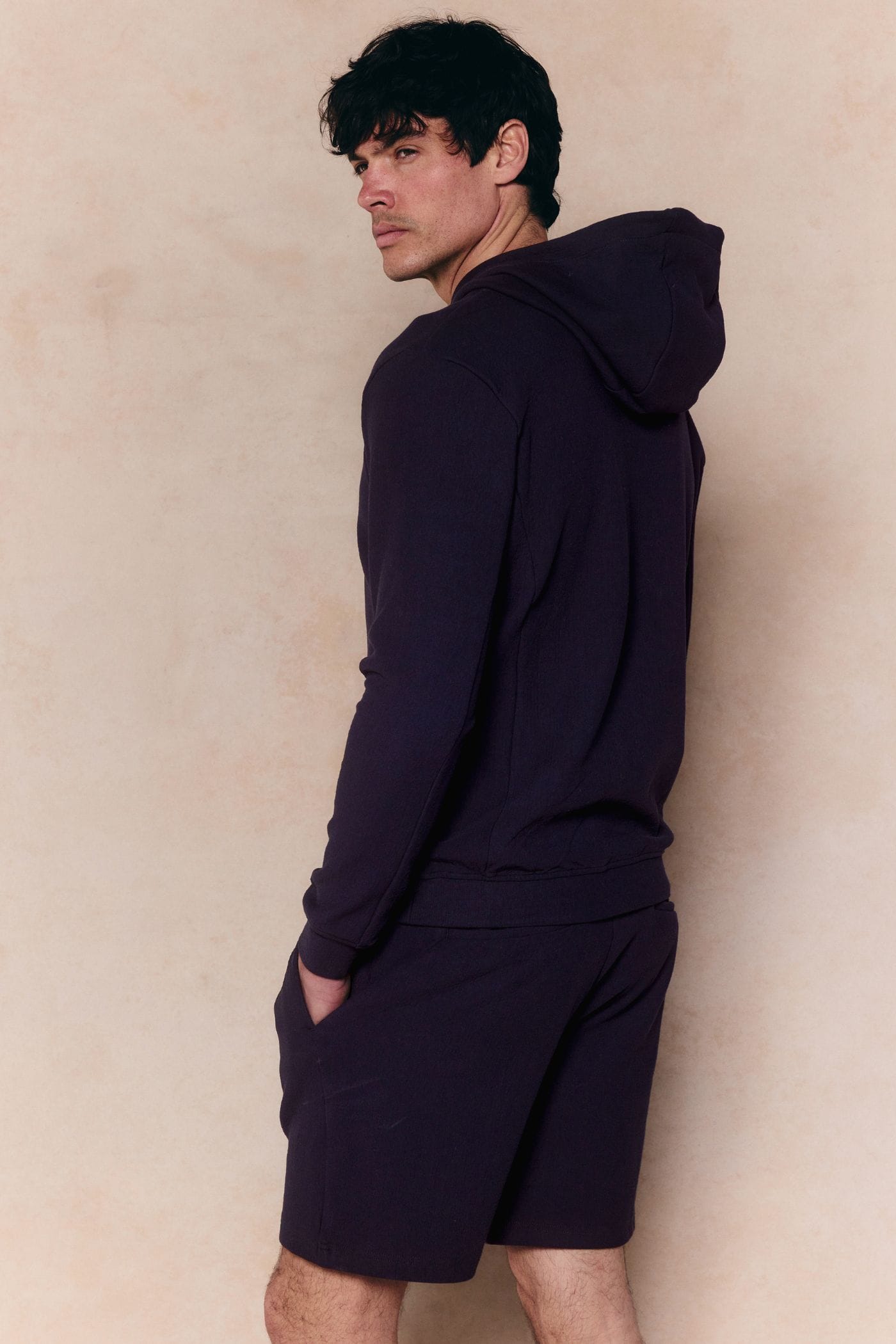 Man in navy Zarco Crinkled Jersey Hoodie and matching shorts, looking over his shoulder.
