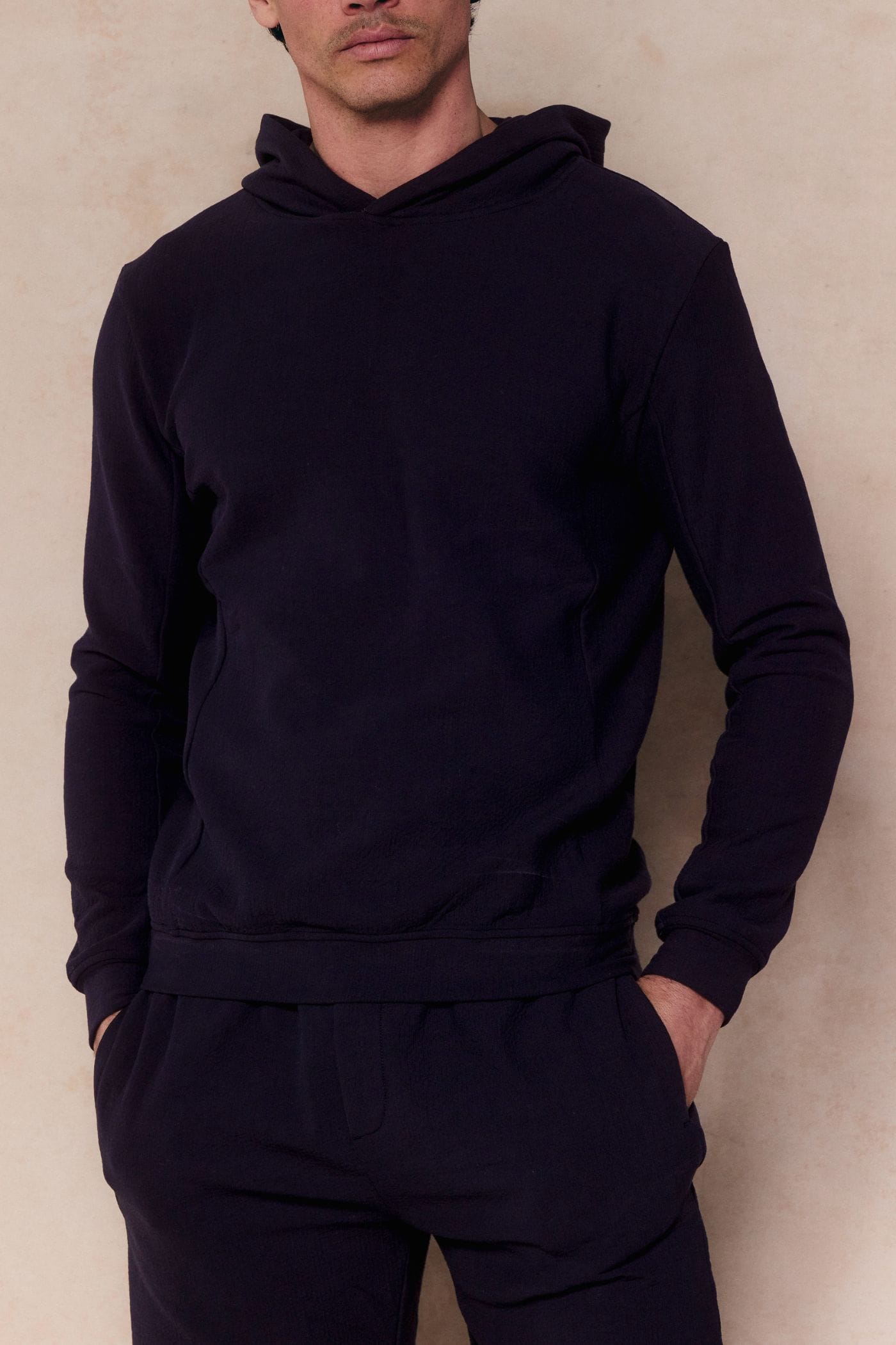 Man in a navy Zarco crinkled jersey hoodie and matching pants, hands in pockets.