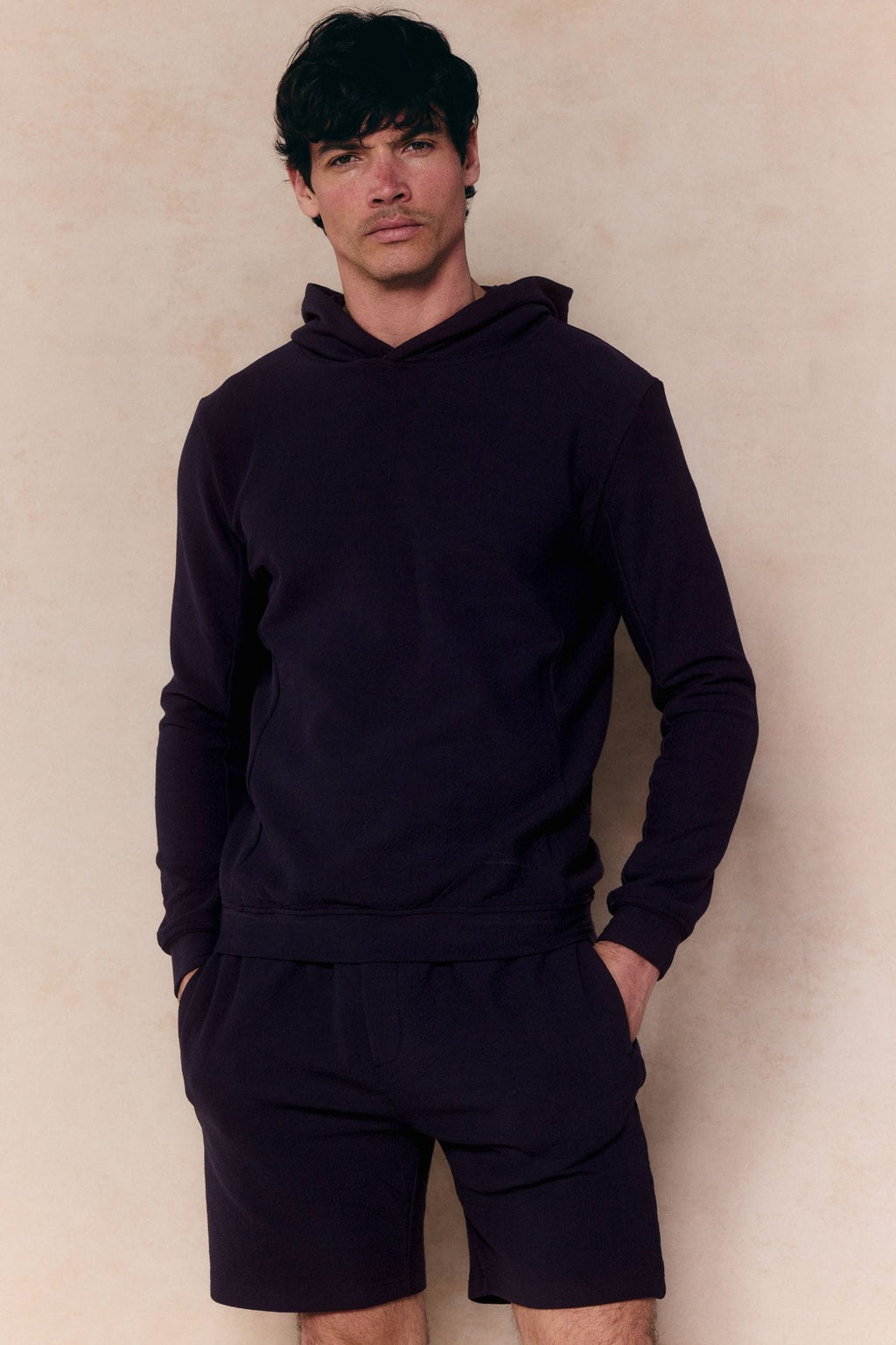 Man wearing a navy Zarco Crinkled Jersey Hoodie and matching shorts, hands in pockets.