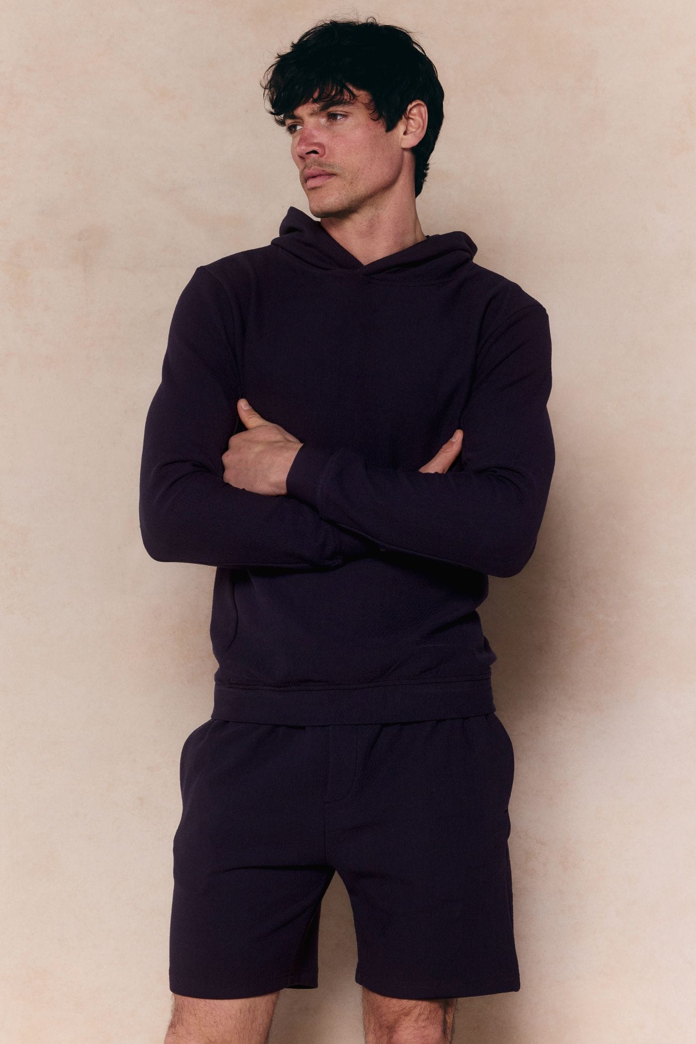 Man in navy Zarco Crinkled Jersey Hoodie and matching shorts, arms crossed, looking left.