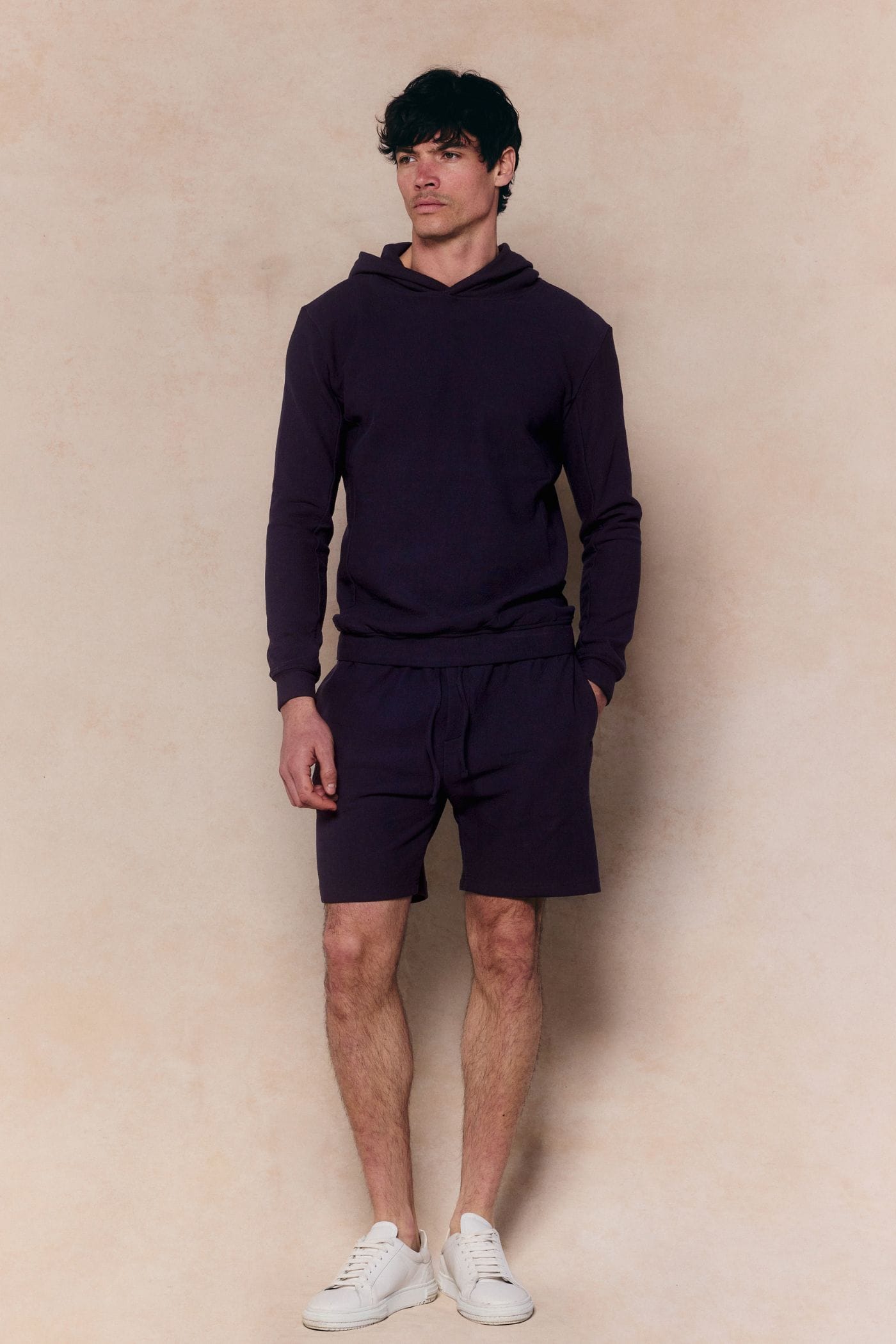 Man in a navy Zarco Crinkled Jersey Hoodie and matching shorts, with white sneakers.