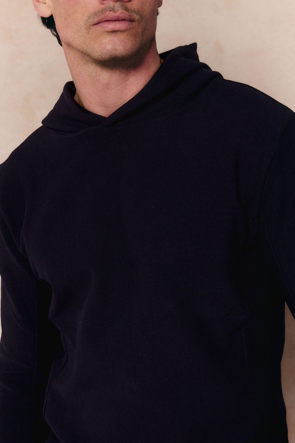 Man in a navy Zarco crinkled jersey hoodie, showing the textured fabric and hood detail.