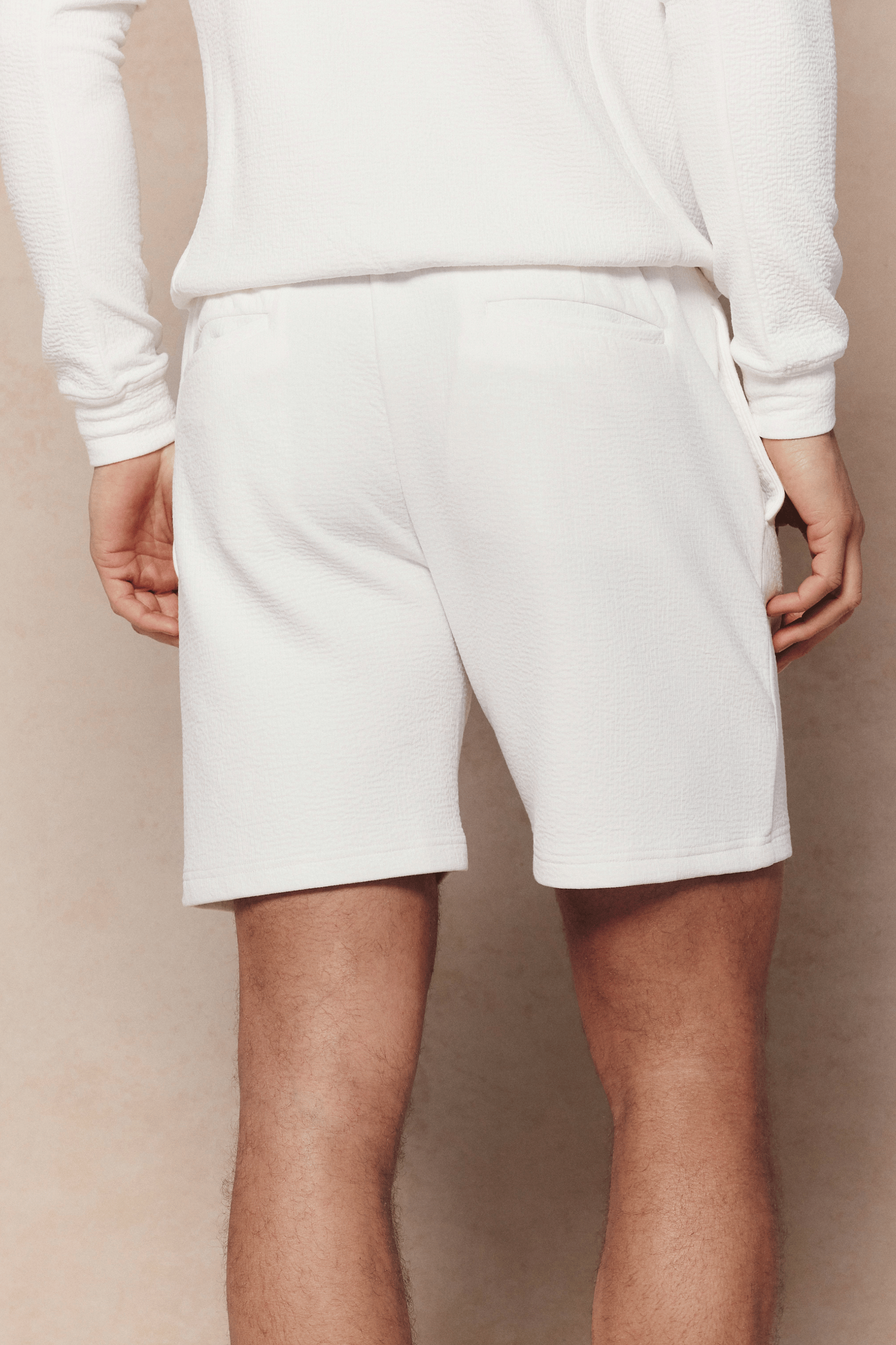Rear view of a person wearing ivory Zarco crinkled jersey shorts with a matching long-sleeve top.