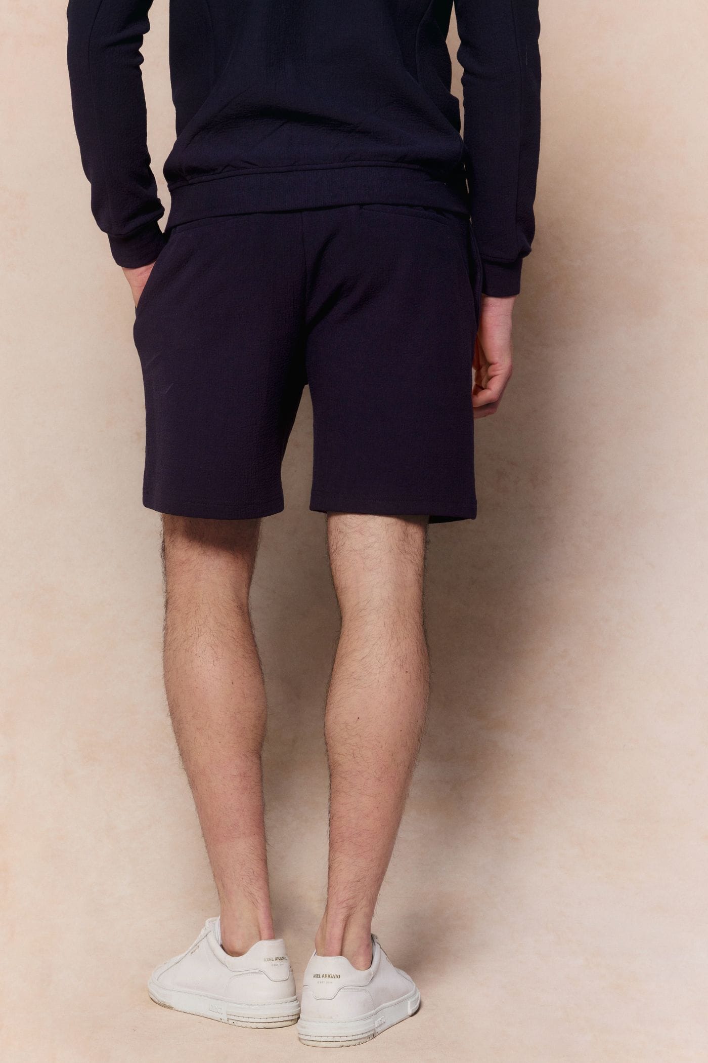 Man wearing navy Zarco crinkled jersey shorts and matching long-sleeve top, with hands in pockets.