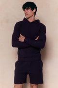 Man wearing a navy crinkled jersey short and matching hoodie, arms crossed.